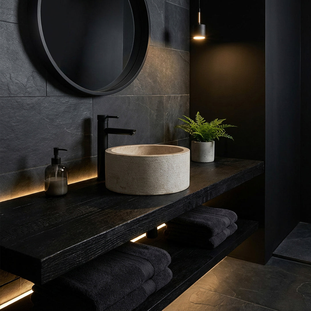 Runt tvättställ i en elegant marmorlook på en mörk träkonsol, iscensatt i ett minimalistiskt mörkt badrum.