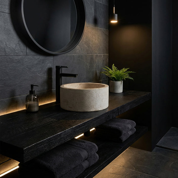 Runt tvättställ i en elegant marmorlook på en mörk träkonsol, iscensatt i ett minimalistiskt mörkt badrum.