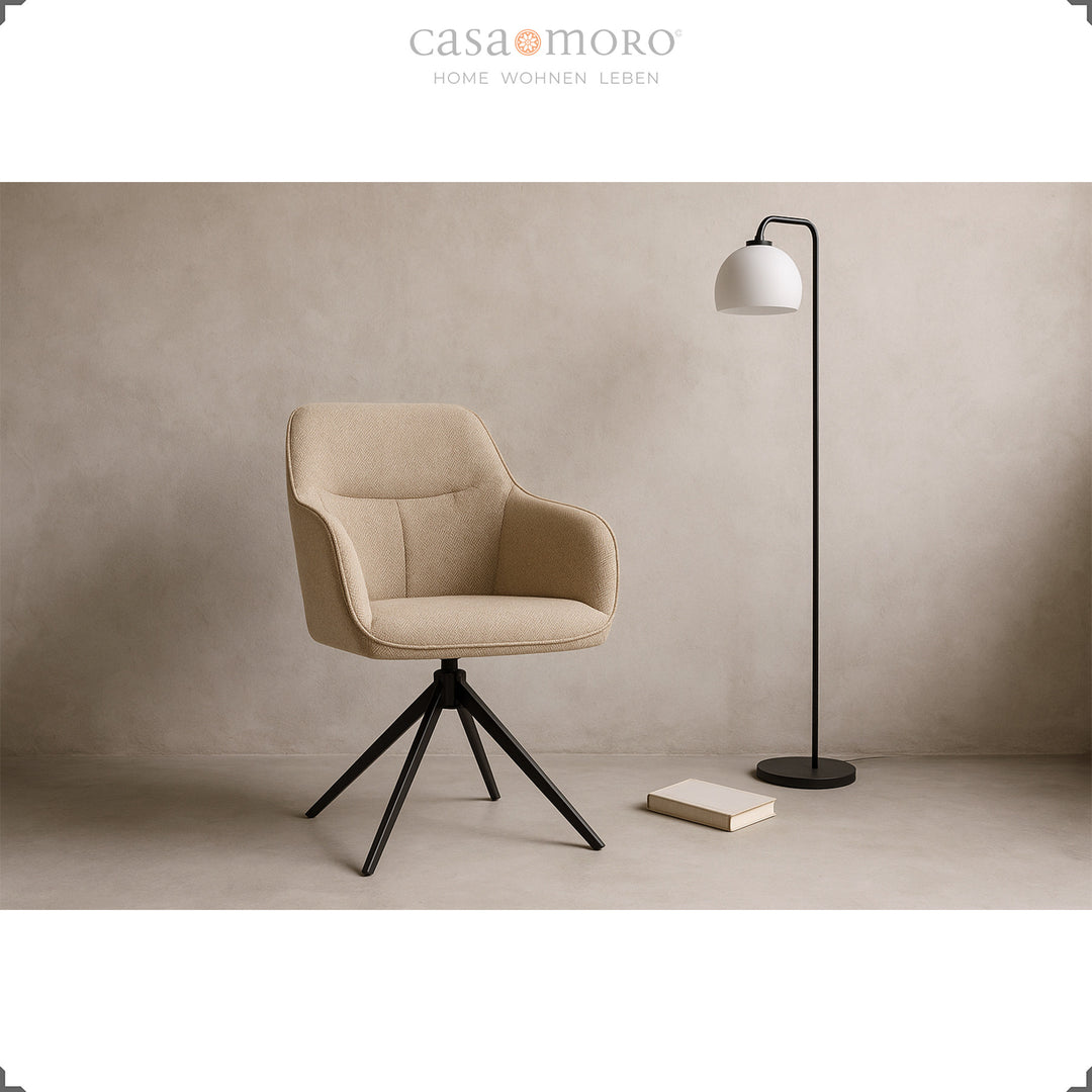Modern 360° roterande klädd stol med armstöd i beige, iscensatt i vardagsrummet med en svart golvlampa och bok på ett ljust golv