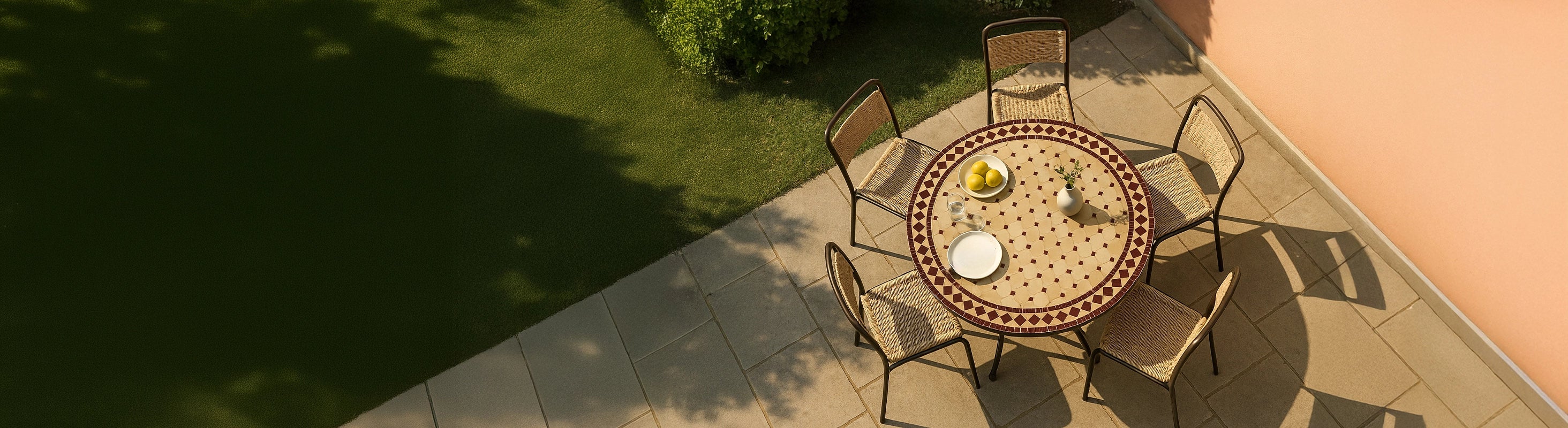 Mosaikbord Ø100 – Stort runt mosaikbord Ø100 cm med zellige kakel och flera stolar på terrassen i trädgården från fågelperspektiv med varm sol