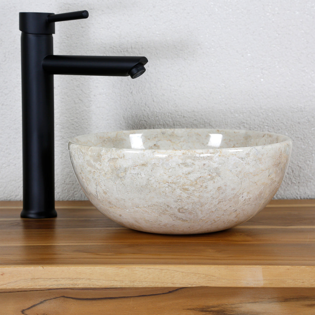 Tvättställ i ljus marmor på träskiva med svart beslag i en tydlig, minimalistisk studiomiljö
