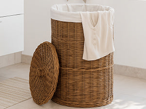 Hög brun tvättkorg i rotting med ljus tvättsäck och beige duk i badrummet, med locket stående framför
