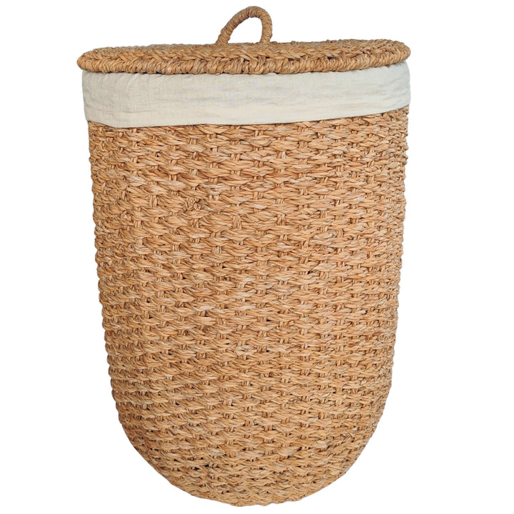 Öppen tvättkorg av naturfärgat sjögräs med en ljus tyginsats och ett lock som vilar mot sidan.